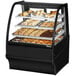 A True curved glass black dry bakery display case on a counter filled with various pastries.