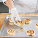A person wearing gloves putting cinnamon rolls on a Chicago Metallic wire in rim sheet pan.