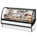 A True refrigerated bakery display case full of different cakes with curved glass.