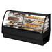 A True 77 1/4" Curved Glass Black Dual Service Refrigerated Bakery Display Case on a counter with different types of pastries.
