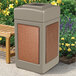 A beige StoneTec square trash can with Sedona panels next to a wooden bench.