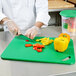 A chef cutting vegetables on a green Rubbermaid cutting board.