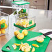 A Rubbermaid green cutting board with lemons and a knife on it.