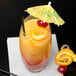 A highball glass filled with an orange drink and a yellow umbrella with a cherry on top.