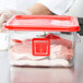 A person holding a Rubbermaid red square food storage container lid filled with meat.