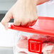 A person putting meat into a red Rubbermaid food storage container.