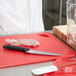A chef using a knife to cut meat on a red Rubbermaid cutting board.