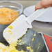 A person using a white Rubbermaid silicone spatula to cut food on a pan.