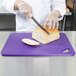 A person cutting bread on a purple Rubbermaid cutting board.