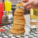 A hand holding a stainless steel tower of onion rings.