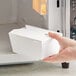 A hand holding a small white microwavable folded paper take-out box.