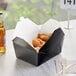 A black Choice folded paper take-out box filled with fried chicken on a table.