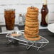 A Clipper Mill stainless steel rack holding a stack of fried onion rings with a ramekin of sauce on a table.