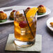 A Reserve by Libbey Modernist Rocks glass of whiskey with ice and a cherry on a napkin.