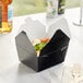A black Choice microwavable paper take-out box with food inside.