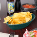 A basket of chips on a table with a bowl of salsa.
