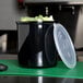 A black Carlisle round plastic crock with broccoli in it and a lid on a counter.