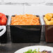 A Tablecraft black bowl filled with shredded carrots on a table with other bowls of food.