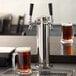 A glass of beer next to an Avantco 2 tap tower with a silver column.