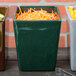 A green Tablecraft square container with white speckles holding shredded carrots on a counter with a group of square containers of food.