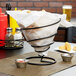 A Clipper Mill black iron wire cone basket on a table with a bowl of sauce in it.