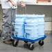 A man pushing a cart with four blue Vollrath Traex ice totes.