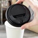 A hand holding a black Choice hot paper cup lid over a white cup of coffee.
