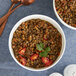 A white bowl of dried green lentils with tomatoes and cilantro.