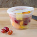 A Pactiv translucent plastic deli container with fruit and red grapes inside.