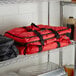 A red ServIt food delivery bag and a black ServIt food delivery bag on a metal shelf.