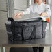 A woman in a chef's uniform using a ServIt black food pan carrier bag.