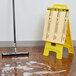 A yellow sign on the floor with black text reading "Caution Wet Floor" next to a mop.