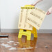 A person using a yellow tool to remove a Rubbermaid box with a stack of paper on a yellow stepladder.