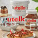 A close up of a Nutella mini glass jar on a table with waffles and strawberries.
