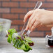 A hand holding a Choice clear plastic serving fork over a salad