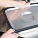 A person holding a black silicone steam table pan band on a metal tray.