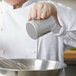 A person in a chef's coat using a Vollrath aluminum shaker to pour powder into a bowl.