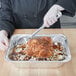 A person holding a Vollrath stainless steel basting spoon over a tray of food.