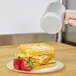 A hand using a Vollrath aluminum shaker to pour sugar onto a plate of waffles with strawberries.