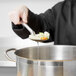A person using a Vollrath perforated stainless steel basting spoon to serve food.