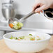 A person using a Vollrath perforated stainless steel basting spoon to serve vegetables from a silver bowl.