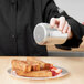 A person holding a silver Vollrath Stainless Steel Shaker over a plate of french toast and strawberries.