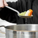 A hand holding a Vollrath perforated basting spoon full of vegetables over a metal bowl.