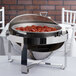 A Vollrath Avenger round roll top chafing dish on a table outdoors with food inside.