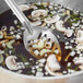 A Vollrath slotted stainless steel spoon serving mushrooms from a pot of soup.