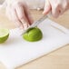 A person slicing a lime on a Choice white bar size cutting board with a knife.
