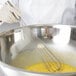 A person using a Vollrath stainless steel piano whisk to mix eggs in a bowl.