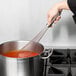 A hand using a Vollrath stainless steel whisk to stir red sauce in a pot.