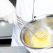 A person using a Vollrath stainless steel whisk to beat eggs in a bowl.