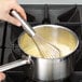 A hand using a Vollrath stainless steel piano whisk to stir a pot of food.
